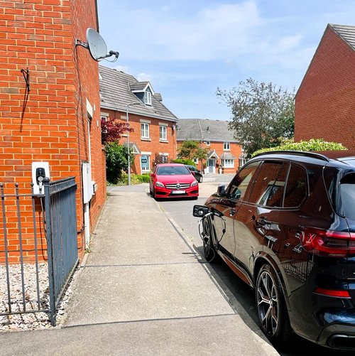 Black BMW car plugged in to a home charger using a pavement channel to keep the cable safe