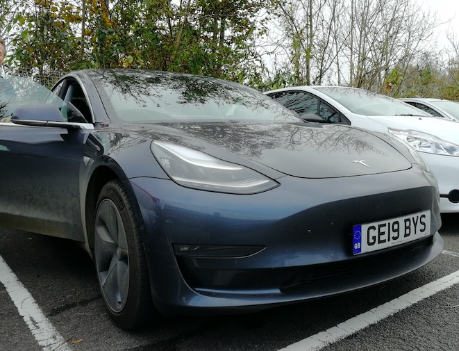 Dark blue Tesla Model 3 full electric four door car, parked with its driver's door open