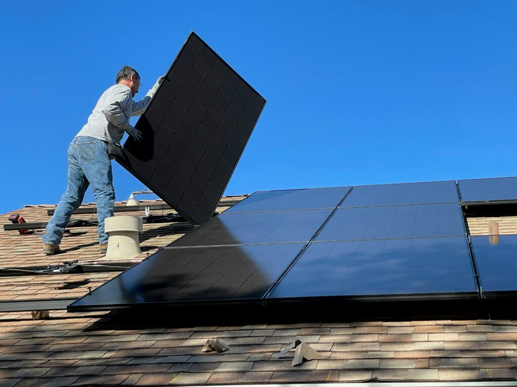 Worker fitting black solar panels on a pitched roof